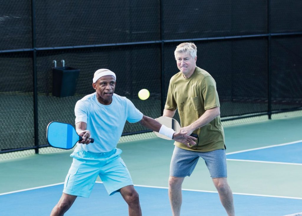 Two men playing pickleball doubles, one man is hitting a forehand