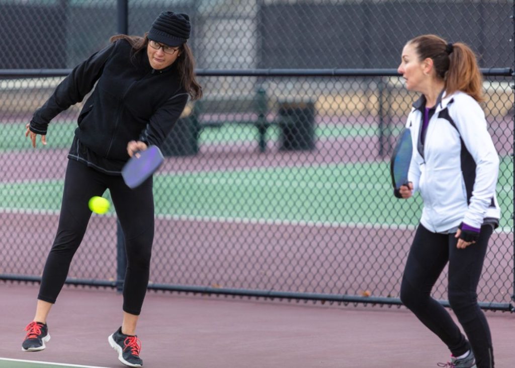 Two women playing pickleball doubles, one woman is hitting a forehand